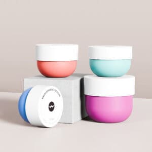 Four colorful bowl-shaped jars (100ml to 500ml) in turquoise, purple, pink, and blue with white lids on a gray block. Chic storage flair!.