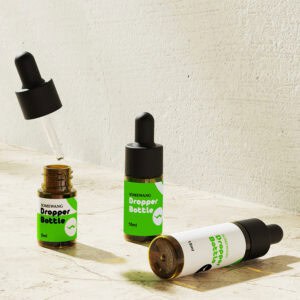 Three green-labeled dropper bottles rest on a textured surface; one is open, droppers above, the others are closed.